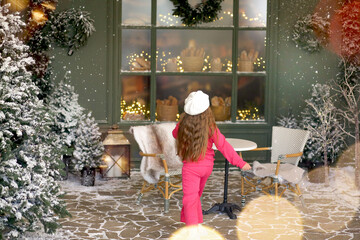 Banner wiht a little girl, seen from behind, near a French bakery. The child is wearing a cozy bright pink outfit and a white beret. Snow-trees, golden lights, Christmas decorations. Copy space
