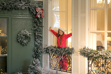 A banner featuring a sweet girl in a pink suit and a milky beret standing on a balcony in a festively decorated room with windows overlooking a cafe terrace. A wonderful mood. A trip for the Christmas
