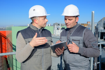 two men looking at tablet stood overlooking an industrial factory