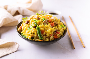 Stewed rice with meat and assortment on vegetables and spices in dark ceramic bowl on white marble table close up. Tasty homemade food concept.
