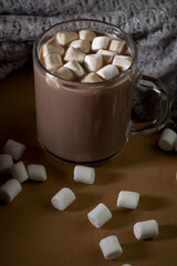 Warm drink with marshmallows in a glass mug on a table with scattered marshmallows around it in the evening light