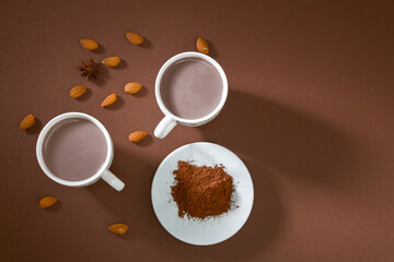 Two cups of hot beverage with cocoa powder and almonds on a brown background during an afternoon gathering in a cozy space
