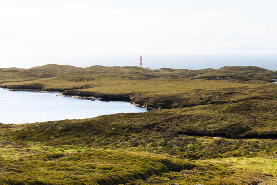 Eilean Glass Lighthouse with soft sunny green meadow and calm sea in foreground, white sky, no clouds
