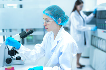 Young Caucasian female scientist in safety gear using micropipette and microscope in modern sterile...