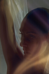 Close-up dancer face and arm in warm atmospheric motion with soft translucent fabric. Concept of beauty editorial campaigns, skincare advertising, emotional portrait branding assets.