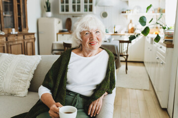 Happy relaxed confident old lady in stylish cardigan enjoying her coffee and retirement relaxing in...