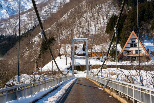 The Suganuma Bridge, a modern suspension bridge providing access to the historic gassho-zukuri village, seen on a clear winter day in Gokayama. Nanto, Toyama, Japan.