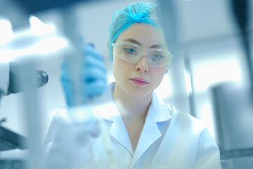 Focused Caucasian female scientist with red hair using micropipette in sterile lab. Young...