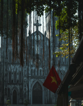 Street view of St. Joseph's Cathedral, concealed in trees and vines, in Hanoi, Vietnam