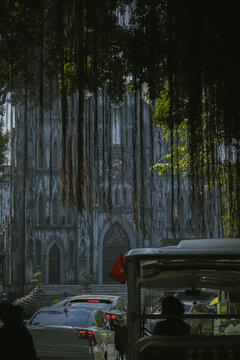 Street view of St. Joseph's Cathedral, concealed in trees and vines, in Hanoi, Vietnam