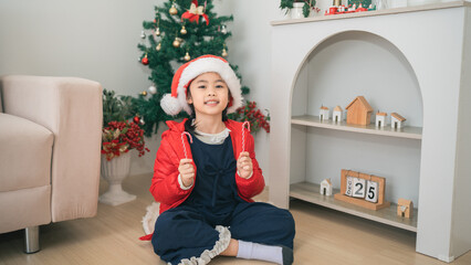 Sweet Joy of Christmas: Child Wearing Santa Hat and Holding Candy Canes in Cozy Living Room Surrounded by Festive Decor and Christmas Tree