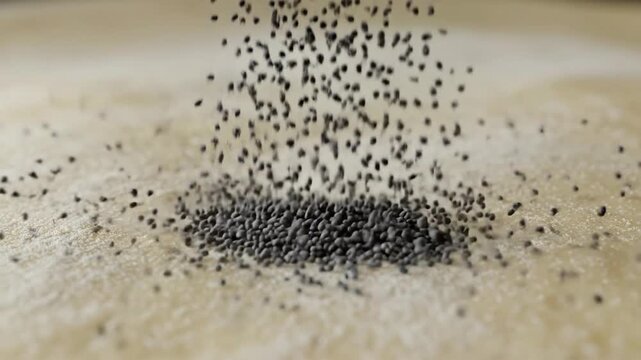 Vantage of black peppercorns dispersing onto a beige surface
