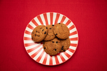 A festive scene featuring chocolate chip cookies on a red-and-white striped plate on red tablecloth