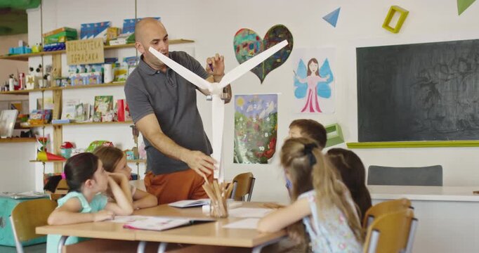 Elementary school teacher explaining wind turbine model to curious children in classroom, STEM lesson on renewable energy, science education and sustainable technology for kids
