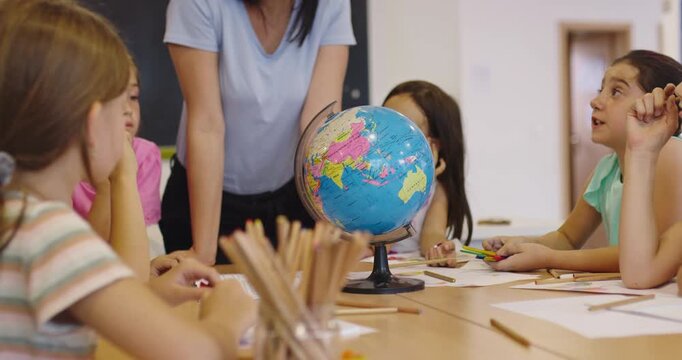 Teacher and elementary students learning geography with globe in classroom, curious children exploring world map together, social studies and global education for kids.