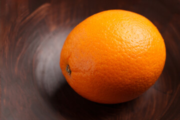 Single ripe orange on dark wooden bowl surface with natural citrus texture. Minimal food still life concept
