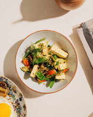 Top view of a fresh salad with leafy greens, radish slices, cucumber, and white cheese cubes on a ceramic plate.