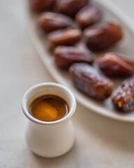 Small cup of coffee served with fresh dates on a plate.