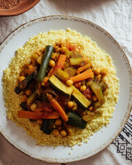 Bowl of moroccan  couscous topped with roasted vegetables and chickpeas on a rustic table.