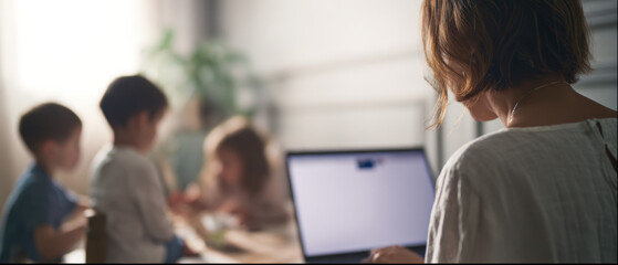 Mother working remotely while kids play nearby
