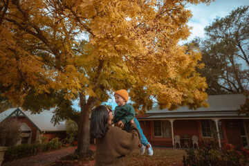 A joyful moment of a mother lifting her cherished child in autumn foliage