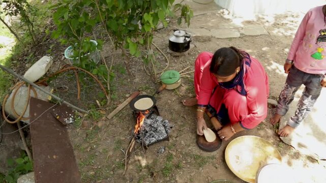 A rural woman prepares chapati using wheat dough during a poor village wedding in Uttarakhand, India. The scene reflects poverty, traditional cooking, community support, and mountain village life.