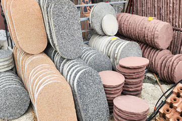 Stacks of circular concrete and stone paving slabs in various colors and textures, displayed at a construction supply yard, representing landscaping materials and outdoor flooring solutions.