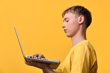 Young learner using a laptop for study and coding on a bright yellow background, focused on screen, keyboard and device, education, digital skills, remote learning, creativity
