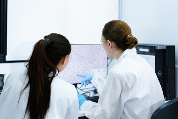 Fototapeta premium Team of female scientists analyzing digital pathology slides on computer. Caucasian and Asian researchers reviewing histology data for medical diagnosis in modern lab.