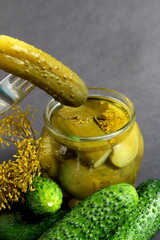 On a gray background there is a glass jar with pickles.	