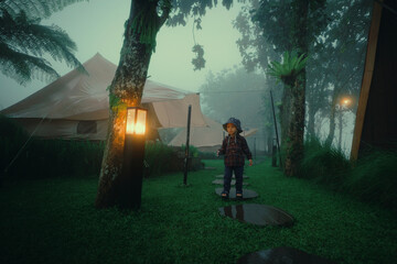 A child walks through a misty forest, passing tents and glowing lanterns.