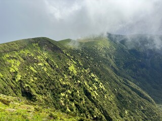 Lush green mountainside covered with dense vegetation under a cloudy sky, showcasing serene natural beauty and misty atmosphere.