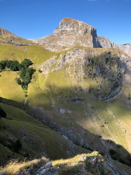 Scenic mountain landscape with rocky cliffs and green slopes under a clear blue sky, perfect for outdoor adventure and nature exploration.