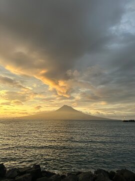 Scenic view of Mount Fuji at sunset over a calm sea with dramatic clouds and warm golden light, capturing Japan's natural beauty and tranquility.