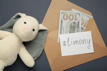 Toy bunny and envelope with word Alimony and money on dark blue background