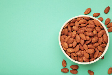 Almonds in bowl on mint background. Whole and dried nuts.
