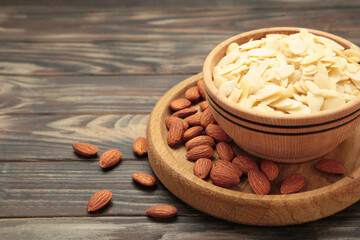 Fresh almond flakes and nuts in bowl on brown wooden background