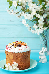 Traditional easter cakes with colorful sprinkles, with eggs, a bunny figurine, and spring flowers on blue background. Vertical photo