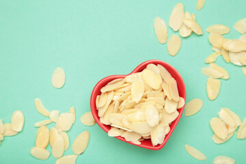 Fresh almond flakes in red plate on mint background