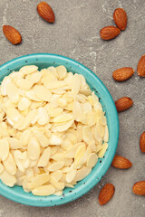 Fresh almond flakes in plate on grey concrete background. Vertical photo