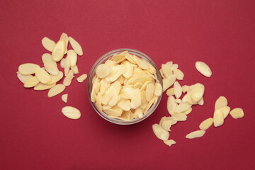 Fresh almond flakes in bowl on red background, closeup