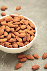 Almonds in bowl on grey background. Whole and dried nuts. Vertical photo