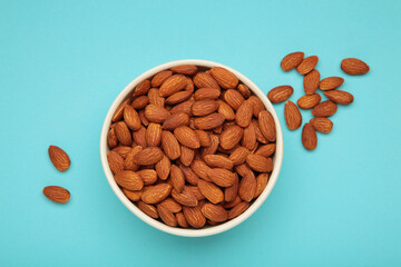 Almonds in bowl on blue background. Whole and dried nuts.