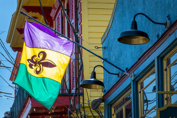 Photo of a Mardi gras flag, purple gold and green flag with a fleur-de-lis hanging on a wall in a street of New Orleans, Louisiana