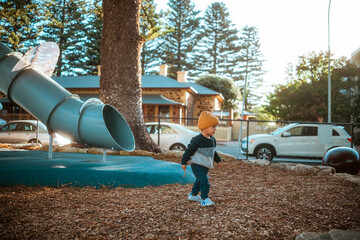 A young child happily enjoys their playtime near a colorful slide in a sunny park