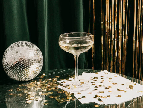 Glass of champagne, glitter and a disco ball at a New Year's Eve party