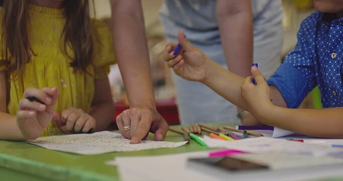 Creative kids during an art class in a daycare center or elementary school classroom drawing with female teacher. 