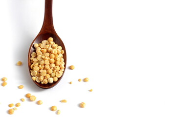 On a white background lies a wooden spoon with dry yellow peas	