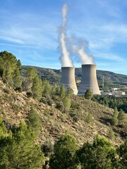 Nuclear power plant cooling towers emitting steam in mountain landscape
