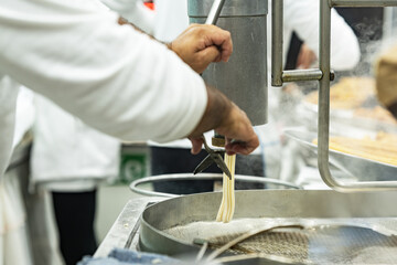 Cook operates a churro maker over hot oil in a busy kitchen; selective focus documents the process, heat and stainless textures of street‑food preparation.
